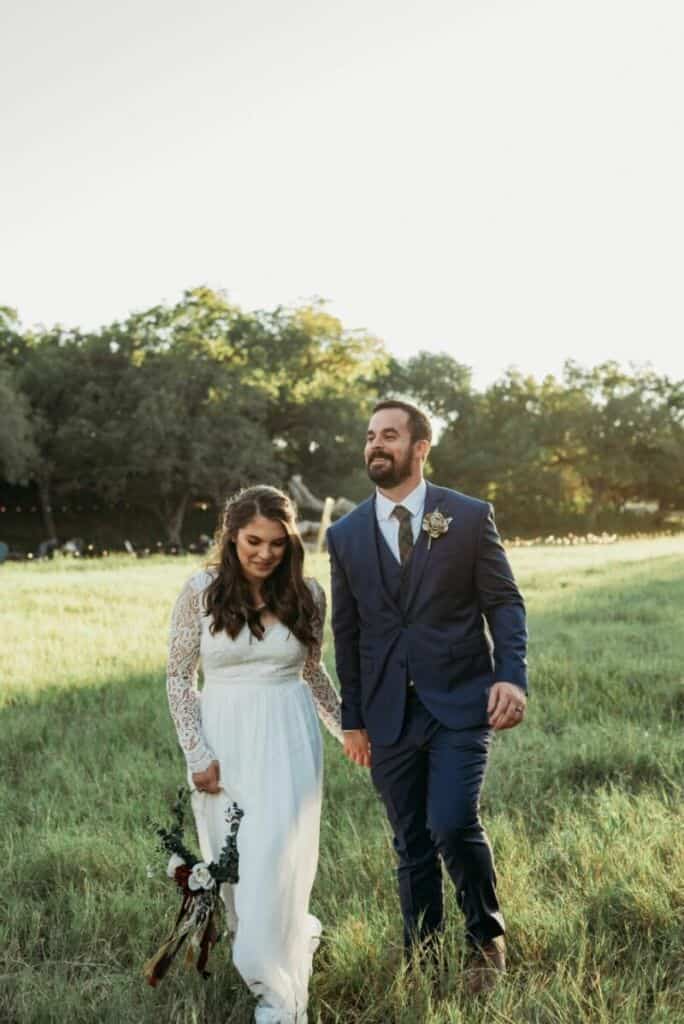 Newlyweds walk through field at Hill Country wedding venue