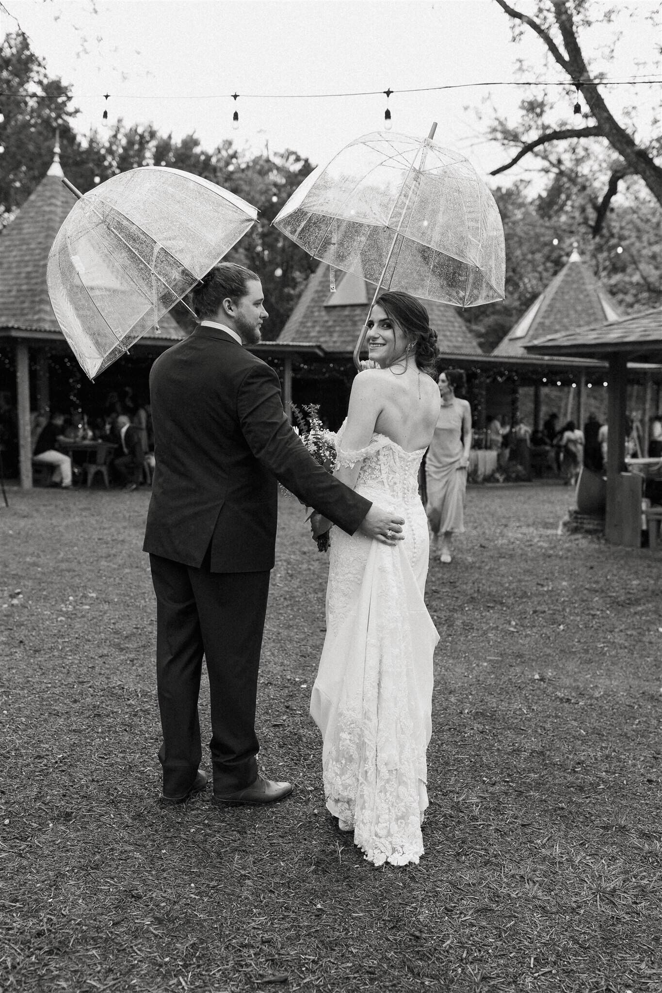 Bride and groom with umbrellas at outdoor rainy wedding in Elm Pass Woods, Texas if you are Outdoor Wedding Planning Texas